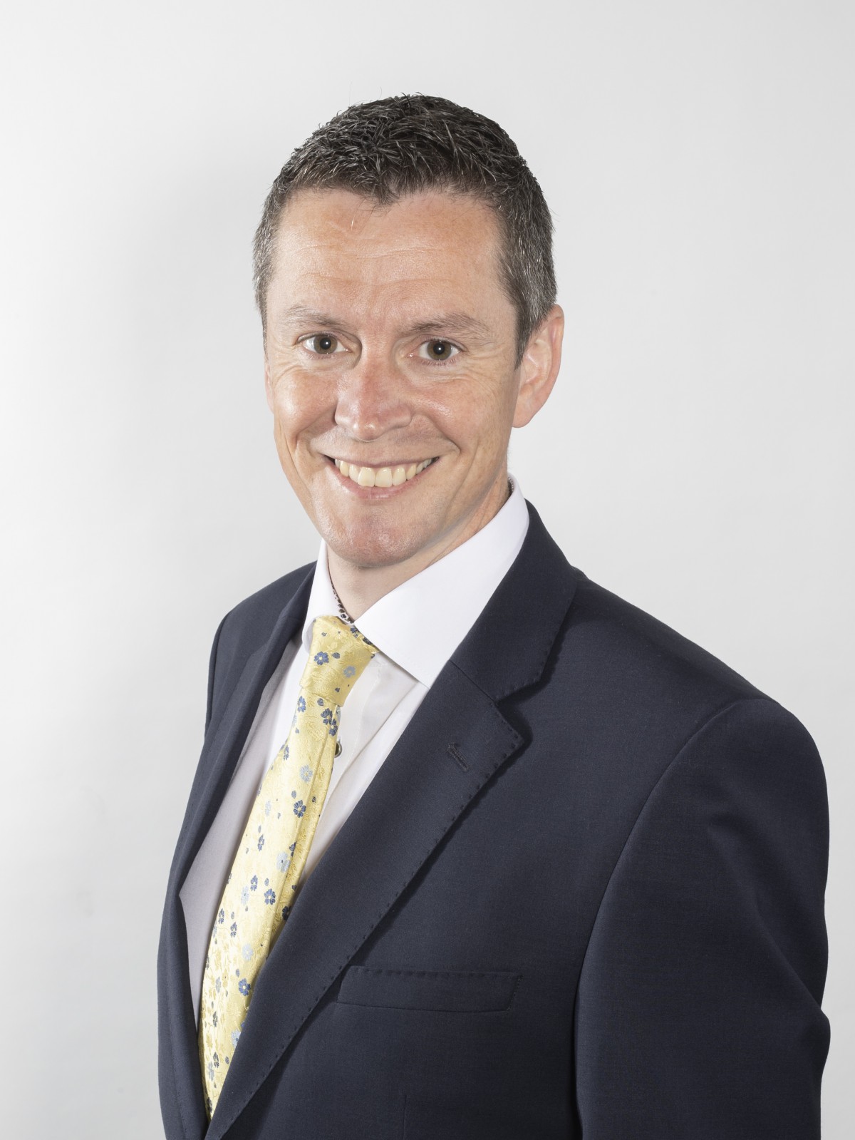 gentleman with dark suit, white shirt, yellow tie and short dark hair